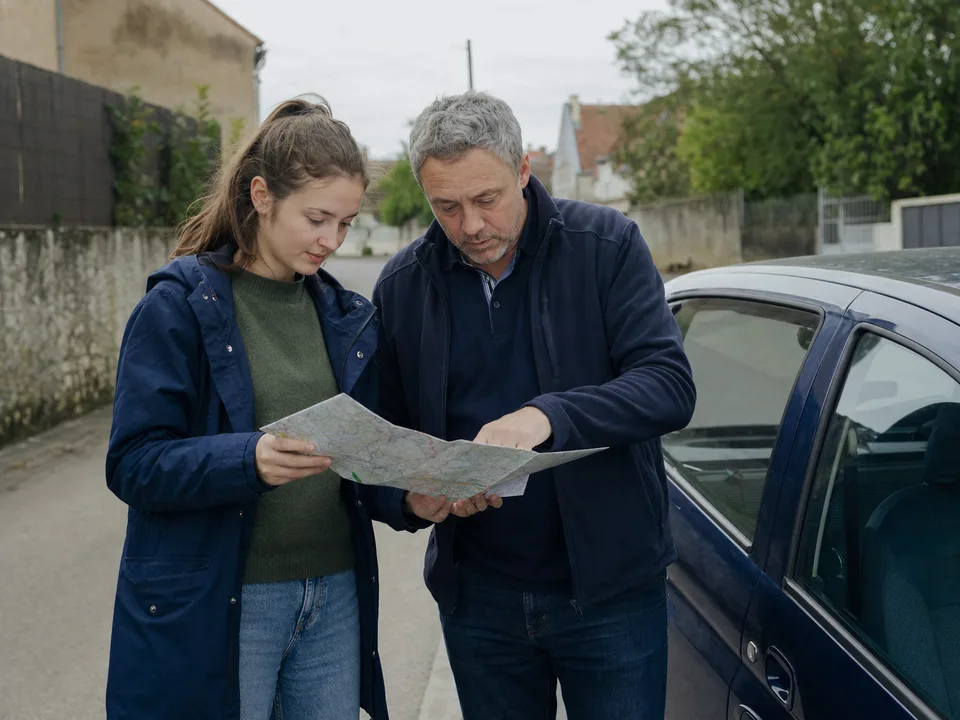 Une jeune conductrice et son accompagnateur préparent un trajet près de leur voiture